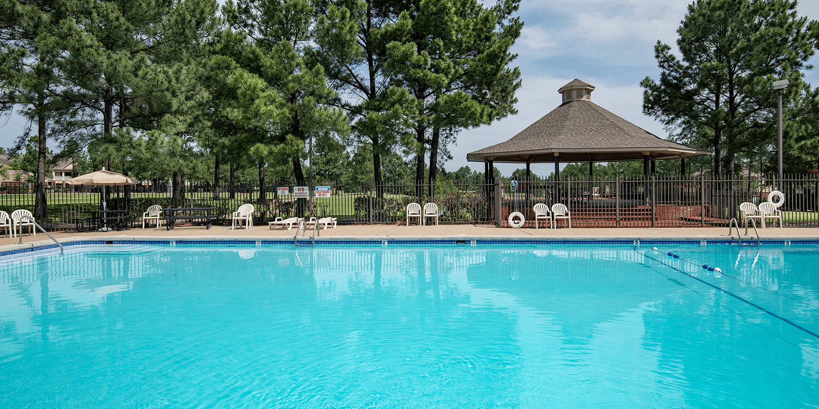 A swimming pool surrounded by trees and a gazebo.